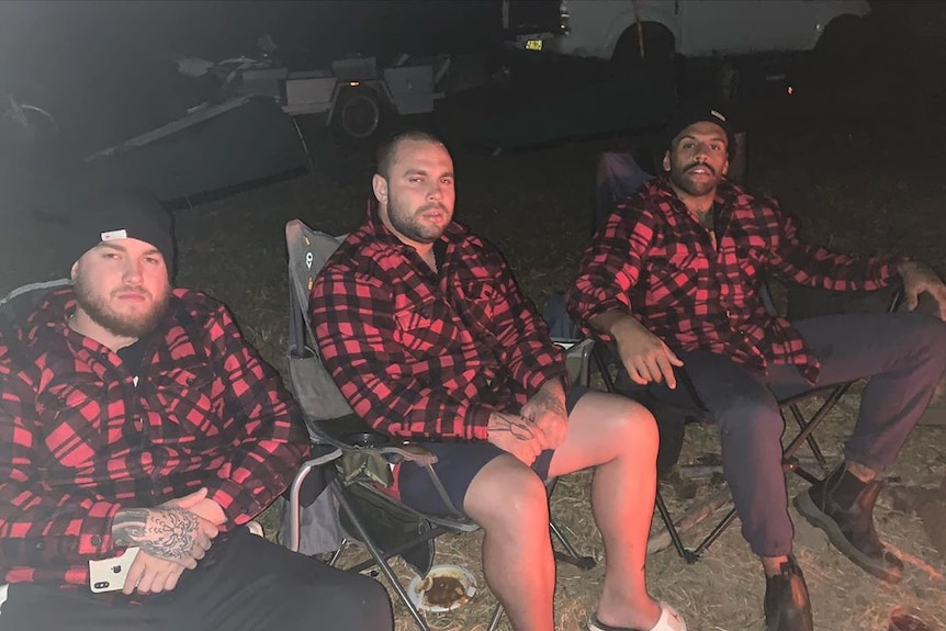 Three guys sit in camping chairs with red and black matching shirts on