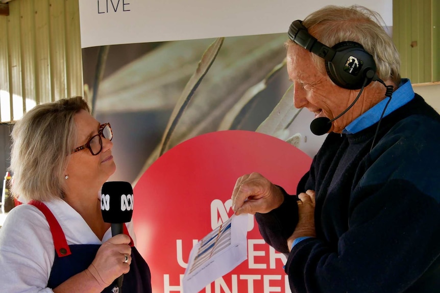 Pritchard with headphones on interviewing woman holding ABC microphone.