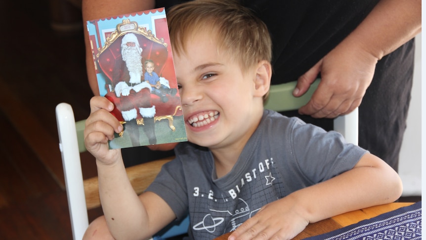 A young boy holds a Christmas card half in front of his face and smiles