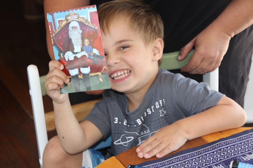 A young boy holds a Christmas card half in front of his face and smiles