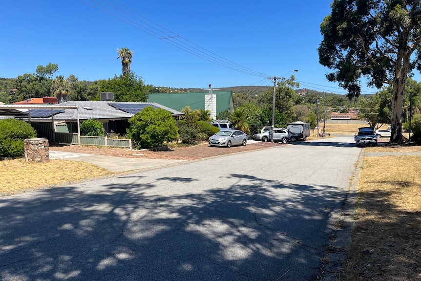 A quiet suburban street with several parked cars near homes. 