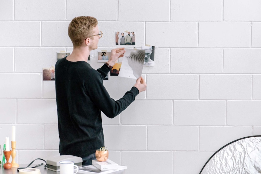 A man puts photographs on a wall, depicting someone redecorating an office.