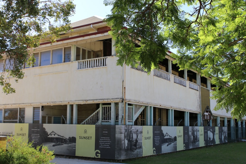 An old two-storey dilapidated hospital building among lush green trees.