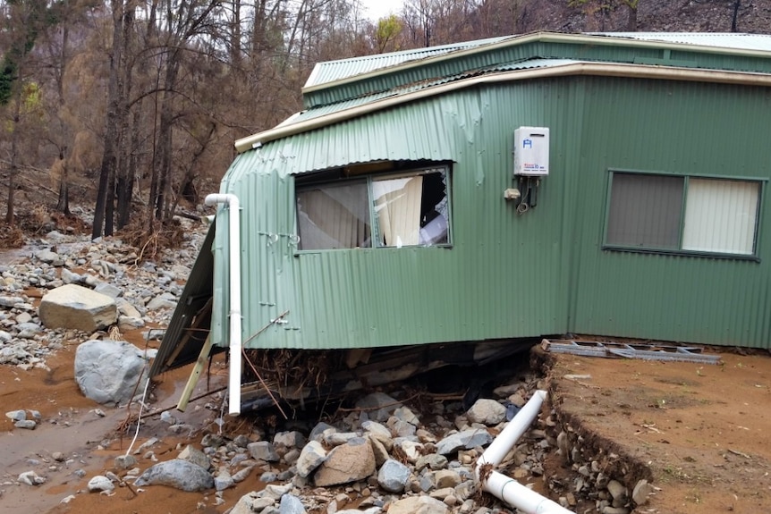 A collapsed green shed with the foundations gone and a deep hole.