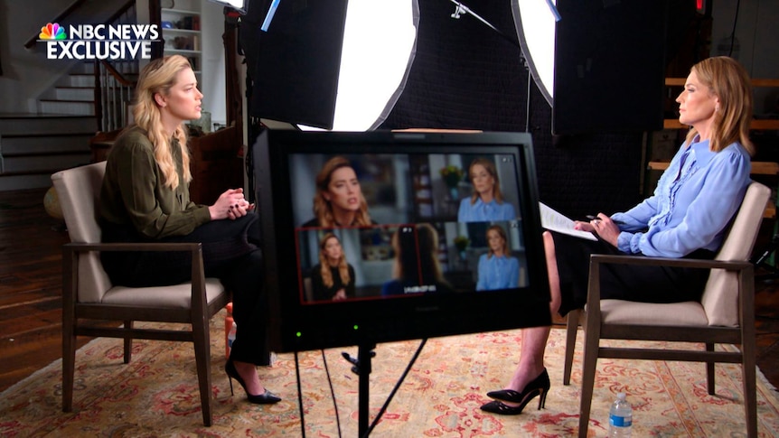 A still image from a TV studio interview shows a female journalist talking with a female actor, with a monitor in the foreground