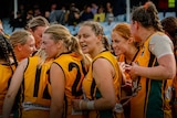 Curtin Uni Wesley players stand arm in arm in a huddle during an Aussie rules match.