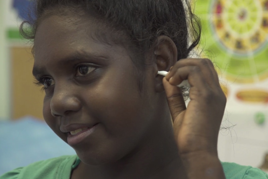 An Aboriginal girl places an earbud into her ear.