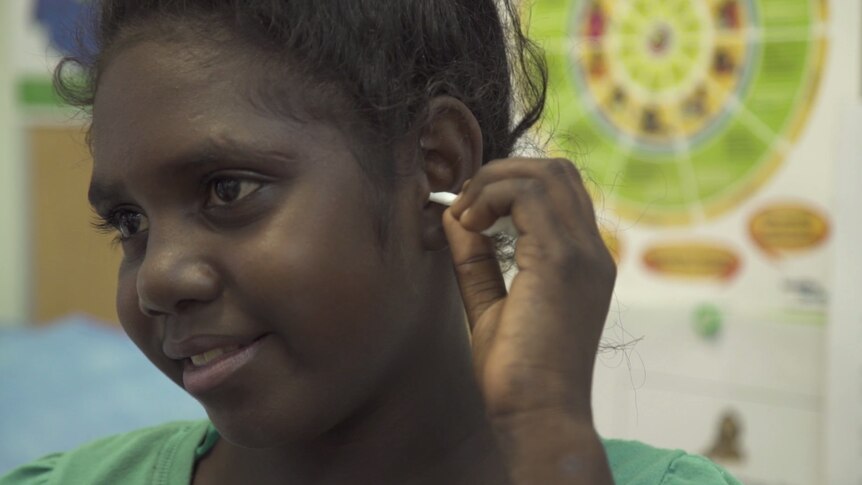 An Aboriginal girl places an earbud into her ear.