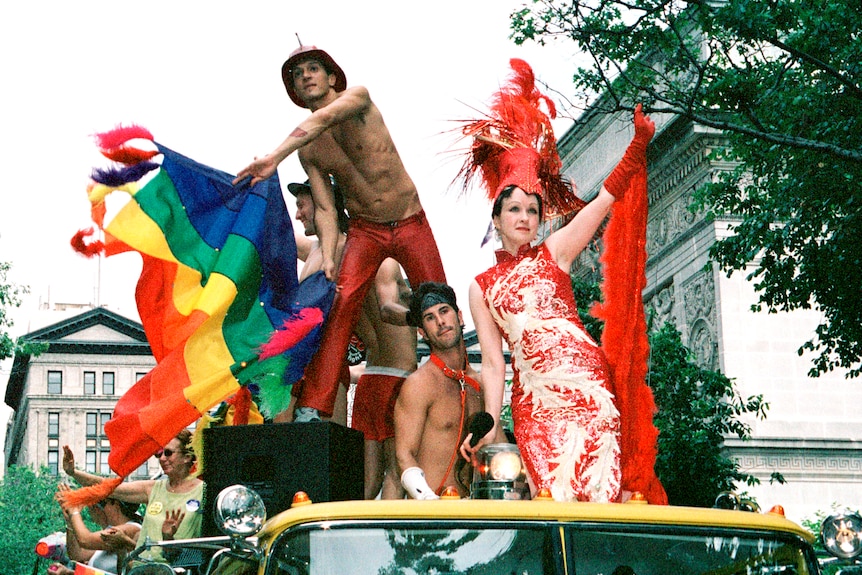Annual Gay Pride Parade, 2001 in New York City. Cindy Lauper and topless men holding rainbow flag riding on top of car.