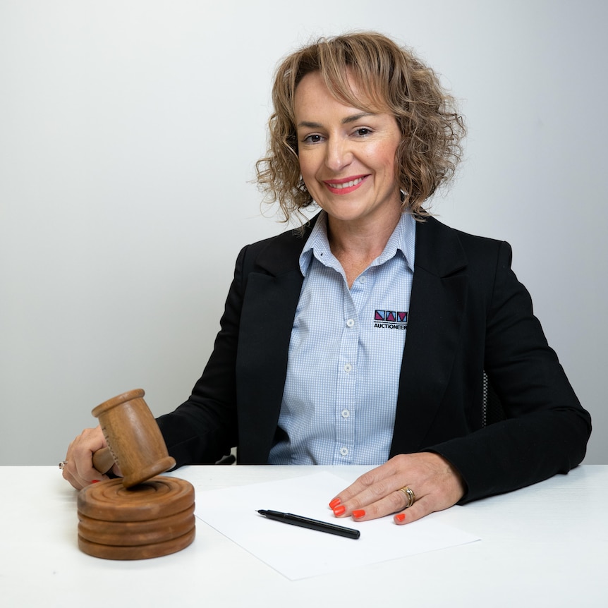 A woman wearing a blazer smiles while holding an auction gavel
