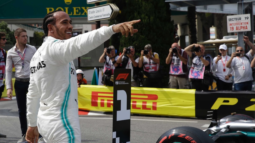 Lewis Hamilton points and smiles wearing his racing overalls.