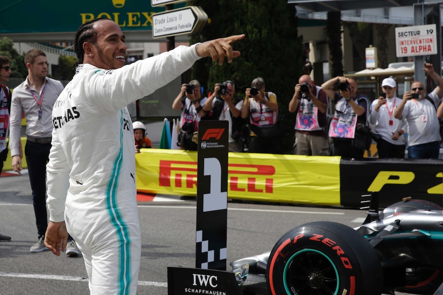 Lewis Hamilton points and smiles wearing his racing overalls.