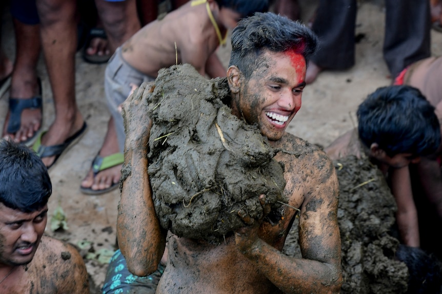 A smiling man hefts a large wad of cow manure. 