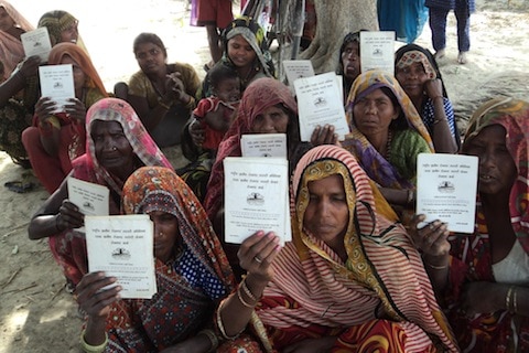 A number of Indian women from the dalit community squat on the ground with voting cards.