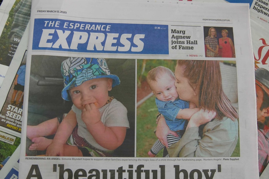 A newspaper with a 15 month old boy wearing a hat and a picture of a woman kissing him