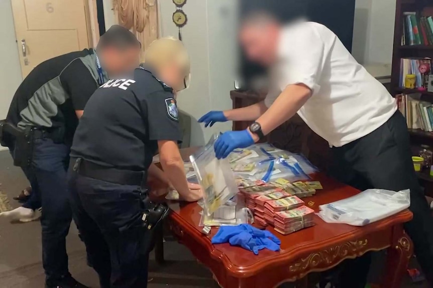 Police leaning over a table stacked with cash. 