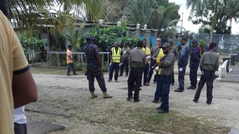 More than a dozen local men stand around at the Manus Island detention centre.