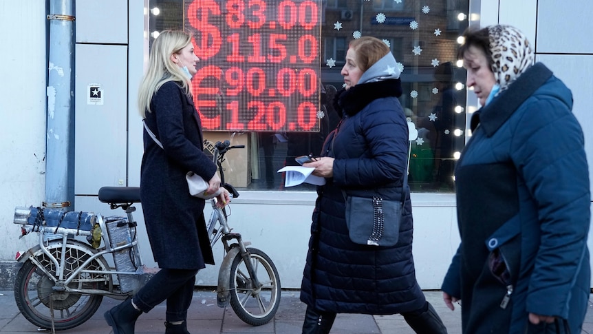 Pedestrians walk past an money exchange displaying very high US Dollar buy and sell rates versus the Rouble.