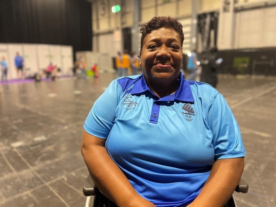A woman wearing a light blue polo sits in a wheelchair and smiles