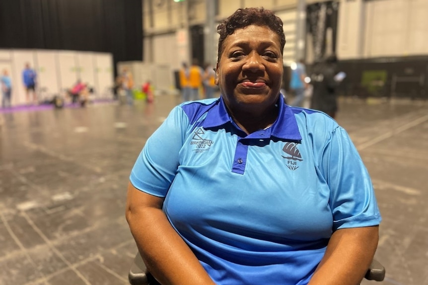 A woman wearing a light blue polo sits in a wheelchair and smiles