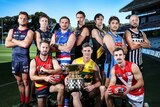 Football players in guernseys crouch behind a premiership cup