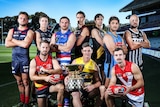 Football players in guernseys crouch behind a premiership cup