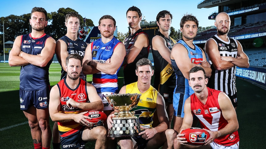 Football players in guernseys crouch behind a premiership cup