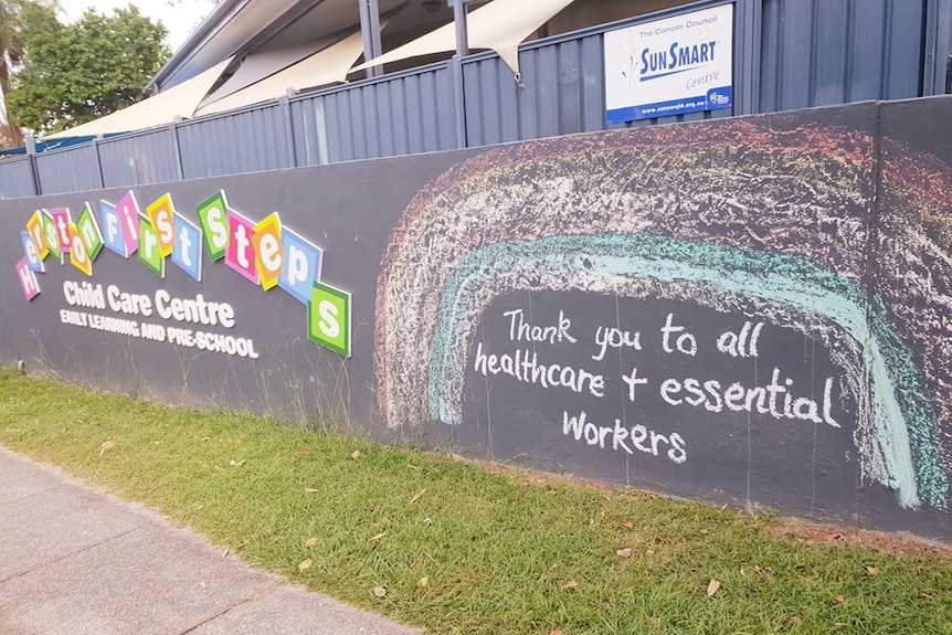 A black wall of a child care centre with a colourful chalk-drawn message.