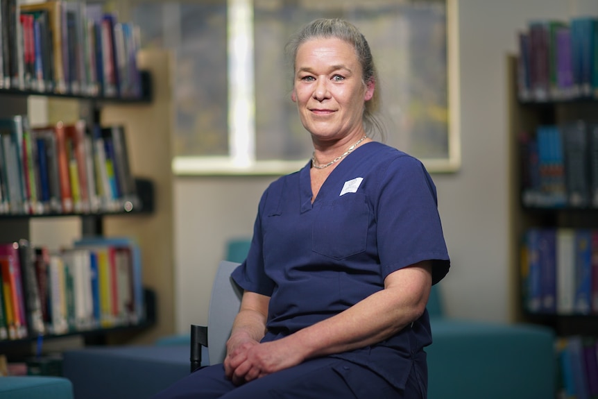 A woman with grey hair wearing blue scrubs in a library