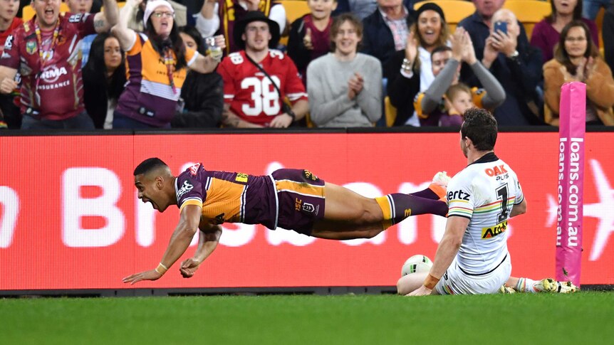 An NRL player flies through the air after planting the ball down for a try.