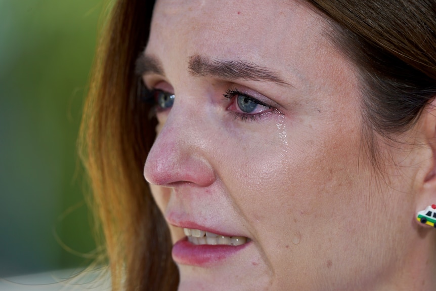 A close up of a woman's face with tears down her cheek. She's wearing ambulance earrings