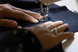 A woman's hands feed fabric through a sewing machine