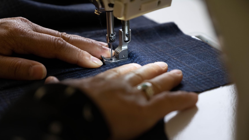 A woman's hands feed fabric through a sewing machine