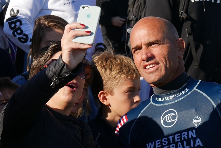 Kelly Slater takes a selfie photo in front of a group of fans.