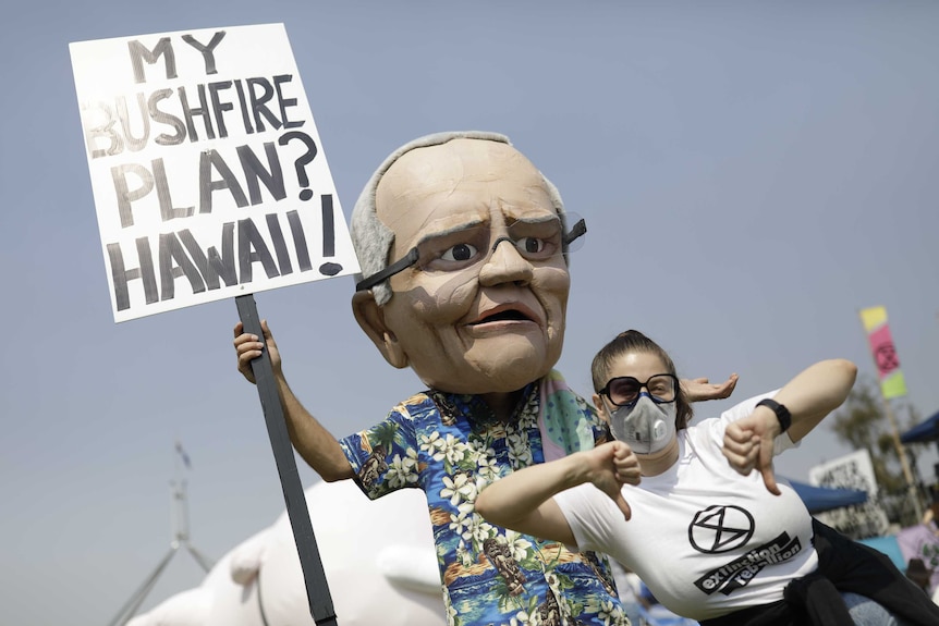 A climate action protester dressed in a Scott Morrison mask and a Hawaiian shirt, holding a placard.