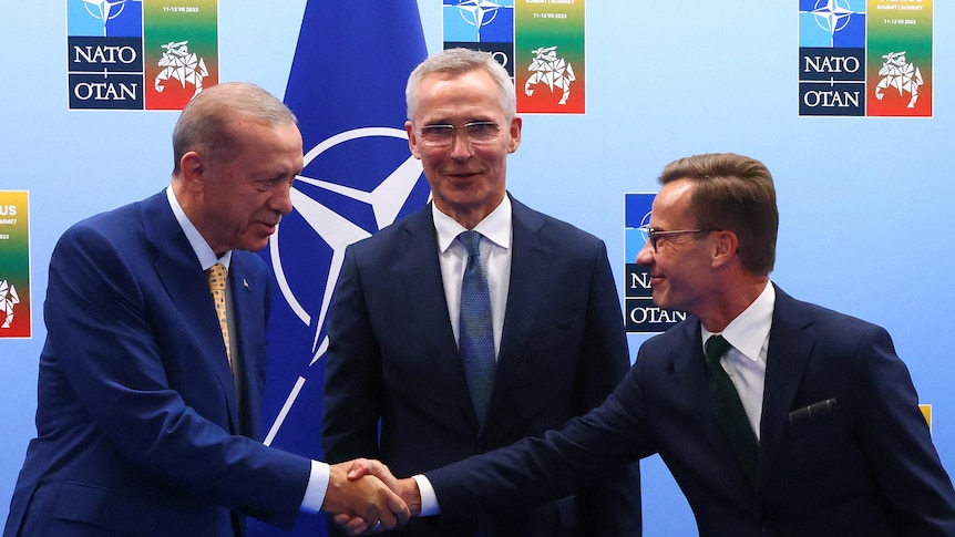 Erdogan and Kristersson shake hands, Stoltenberg stands between them and looks at the camera