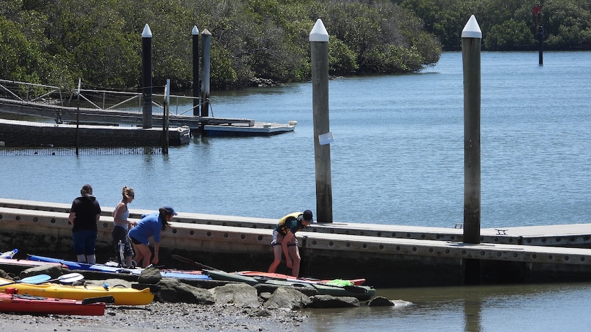 A small sign blown backwards on a pole near people about to go kayaking from a boat ramp