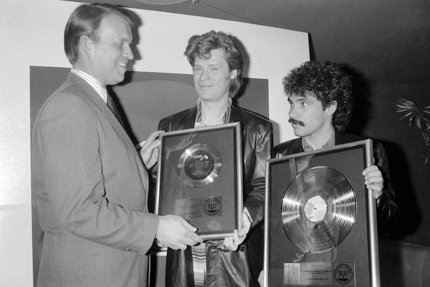 A black and white photo of Daryl Hall and John Oates holding frames with their records in them.