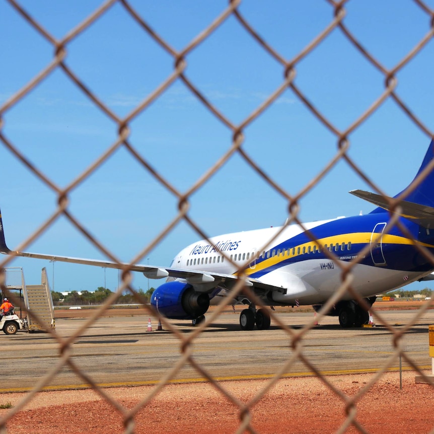 A Nauru Airlines plane sits on an airpot tarmac, viewed through cyclone fencing.
