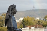 The statue is of a woman in nursing clothing, her hands clasped, Telstra Tower and a rainbow in the background.