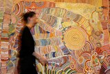 A women passes a colourful artwork by 12 Yunpalara Aboriginal women.