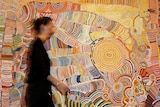 A women passes a colourful artwork by 12 Yunpalara Aboriginal women.