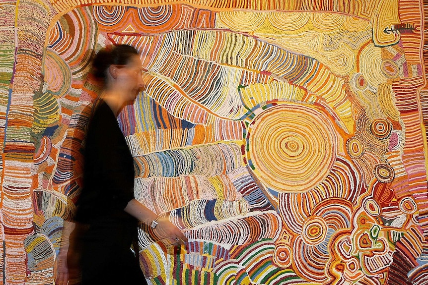 A women passes a colourful artwork by 12 Yunpalara Aboriginal women.