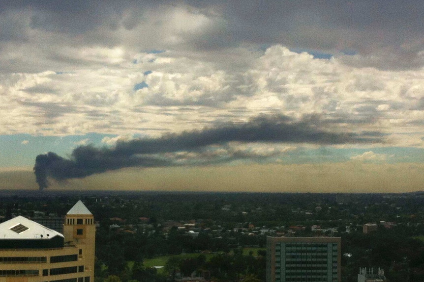 Elevated view from a city building looking across the suburbs to a large plume of smoke moving across the city.