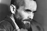 Charles Manson has his head shaved, but still has a long beard. A head shot, he is in profile looking right.