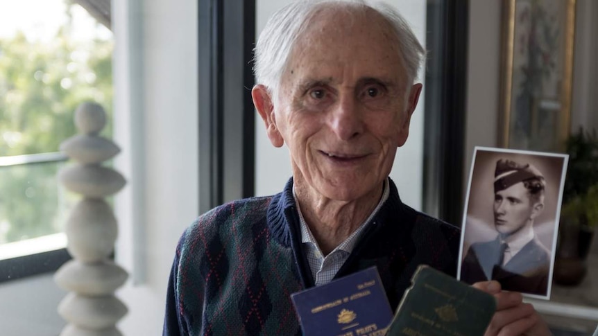 An older man with grey hair holds a photo of his young self as a pilot.