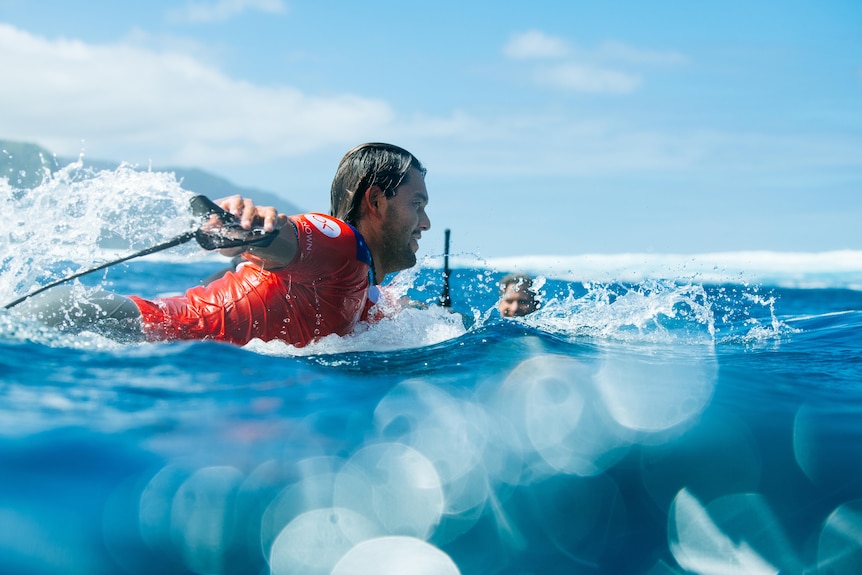 A photo looking through the water at a surfer paddling out from shore before a heat of a competition.