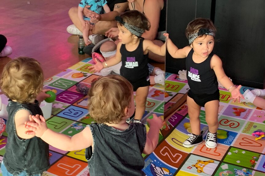 Two toddlers standing on  a baby rug in front of mirror wall at dance classes 