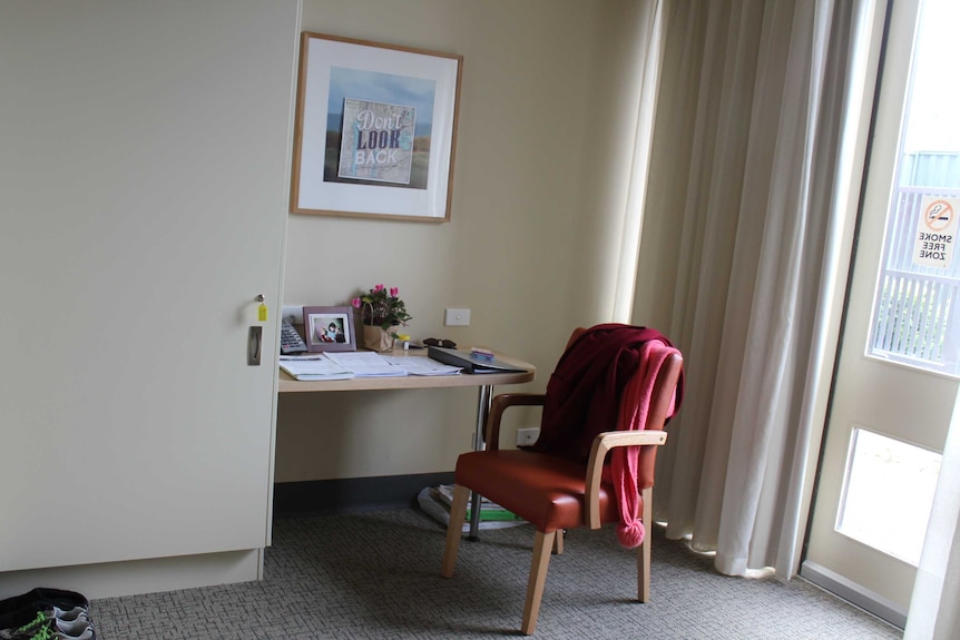 A desk and chair in a grey hospital room beneath a motivational poster that reads: "Don't Look Back".