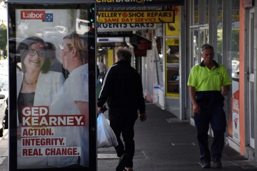 Two men walk past a campaign ad for Ged Kearney as they make their way past the Edwardes Street shops.